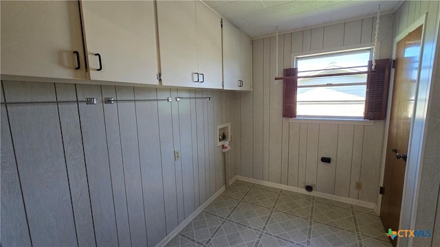 clothes washing area featuring electric dryer hookup, baseboards, wooden walls, washer hookup, and cabinet space