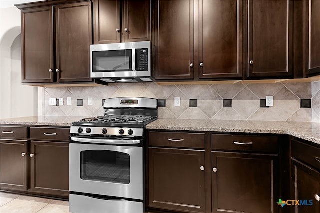 kitchen with light stone counters, light tile patterned flooring, backsplash, appliances with stainless steel finishes, and dark brown cabinetry