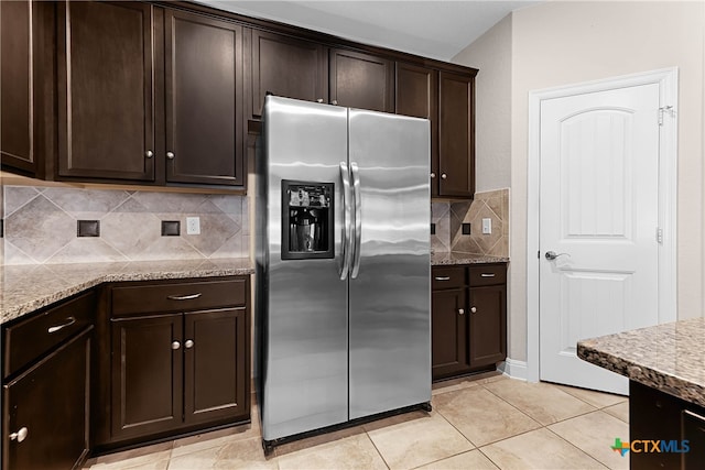 kitchen featuring stainless steel refrigerator with ice dispenser, decorative backsplash, light tile patterned flooring, light stone countertops, and dark brown cabinets