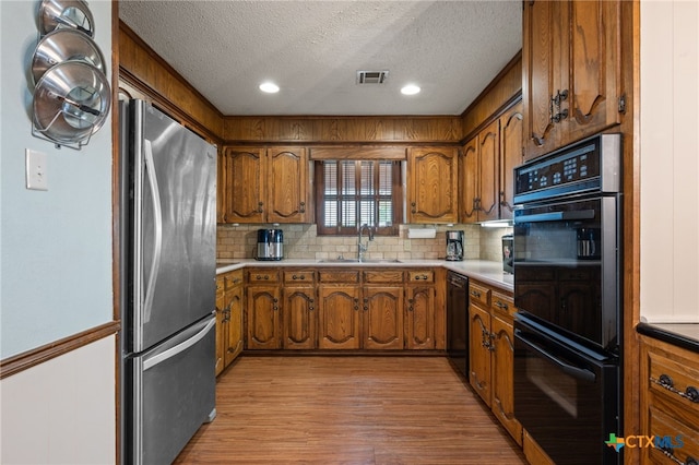 3909 Alderwood Ln, Temple, TX 76502 - kitchen featuring black appliances, a sink, brown cabinetry, a textured ceiling, and tasteful backsplash