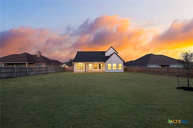 rear view of house with a fenced backyard, board and batten siding, and a yard