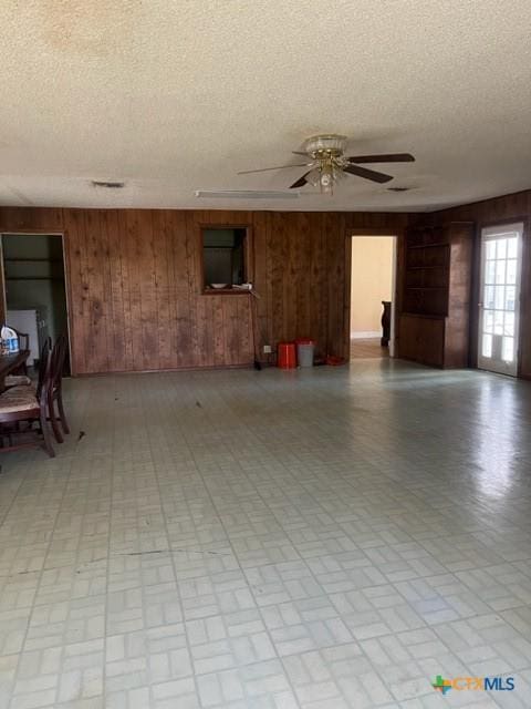 unfurnished room with ceiling fan, wooden walls, and a textured ceiling