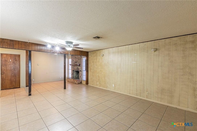 basement featuring wood walls, a brick fireplace, light tile patterned floors, a textured ceiling, and ceiling fan