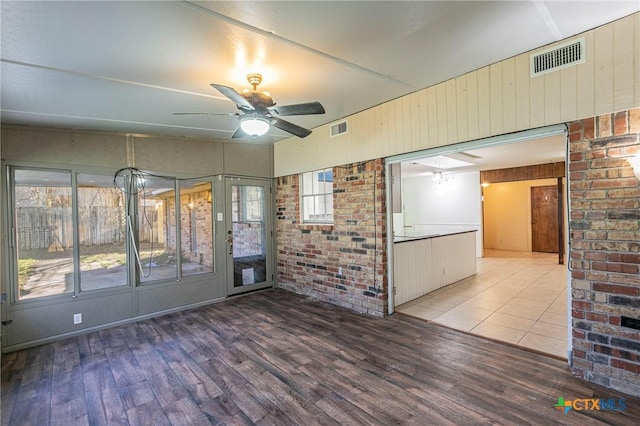 empty room with hardwood / wood-style flooring, ceiling fan, brick wall, and wood walls