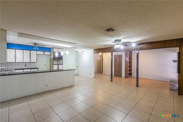 basement with light tile patterned flooring, ceiling fan, wooden walls, and a textured ceiling