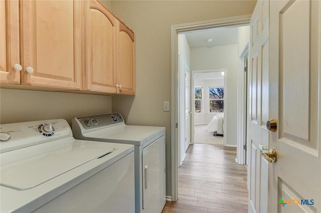 laundry room featuring cabinets, washing machine and dryer, and light wood-type flooring