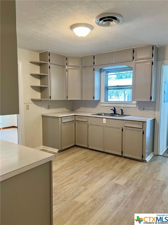 kitchen with gray cabinets, a textured ceiling, sink, and light hardwood / wood-style flooring