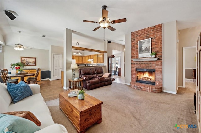 living room featuring a brick fireplace, visible vents, vaulted ceiling, and ceiling fan