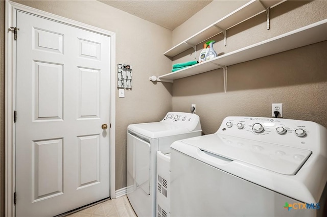 clothes washing area featuring washer and clothes dryer, light floors, a textured ceiling, laundry area, and baseboards