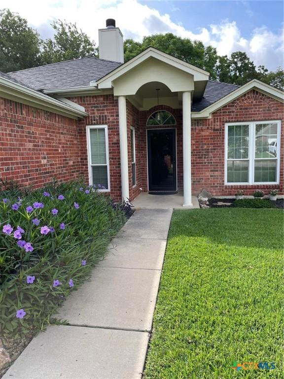 4605 Danbury Dr, Temple, TX 76502 - doorway to property featuring brick siding, a yard, a chimney, and a shingled roof