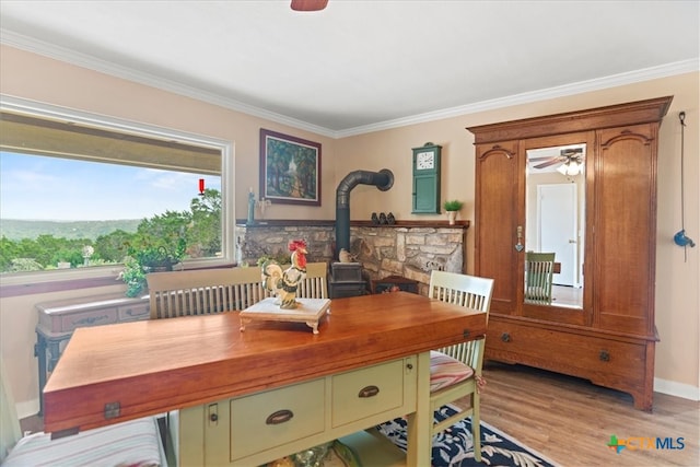 dining room featuring crown molding, a ceiling fan, light wood finished floors, and a wood stove