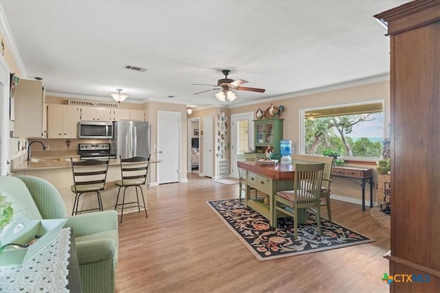 dining room featuring crown molding, a ceiling fan, light wood-style flooring, and baseboards