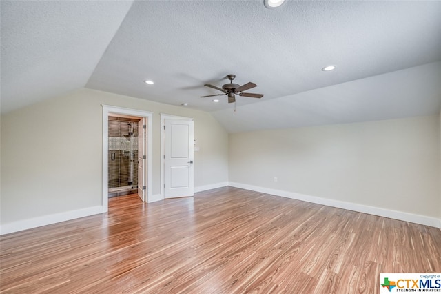 additional living space with a textured ceiling, vaulted ceiling, ceiling fan, and light hardwood / wood-style flooring