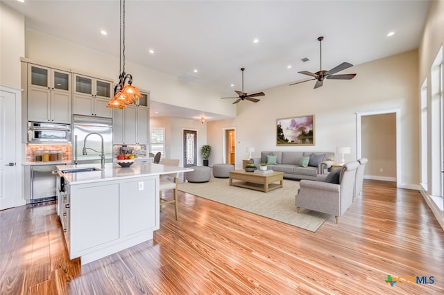 kitchen featuring stainless steel appliances, a center island with sink, ceiling fan, light hardwood / wood-style flooring, and decorative light fixtures