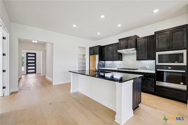 1516 Dancing Oak Ln, San Marcos, TX 78666 - kitchen featuring stainless steel appliances, a sink, a center island with sink, dark countertops, and light wood-type flooring