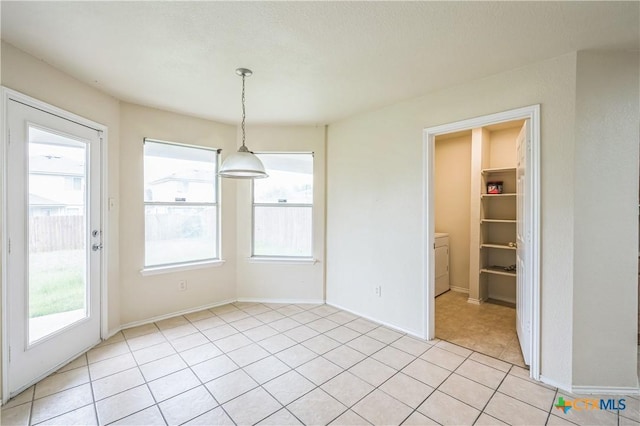 unfurnished dining area featuring baseboards, light tile patterned flooring, and washer / clothes dryer
