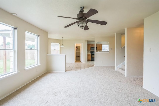 unfurnished living room featuring stairway, baseboards, ceiling fan, and light colored carpet