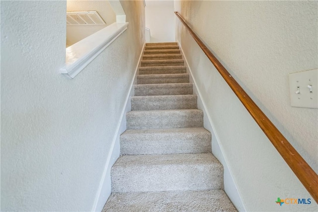 stairs with a textured wall, carpet flooring, and visible vents