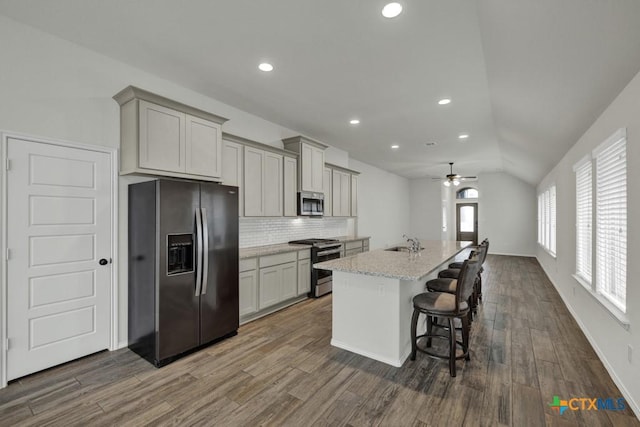 kitchen with stainless steel appliances, an island with sink, light stone countertops, and gray cabinets