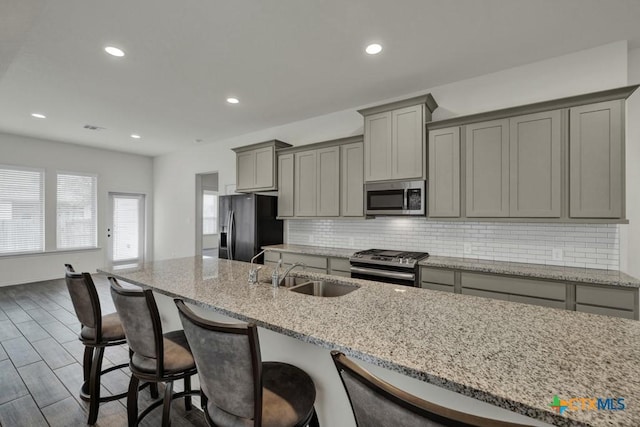 kitchen with sink, gray cabinetry, stainless steel appliances, tasteful backsplash, and light stone countertops