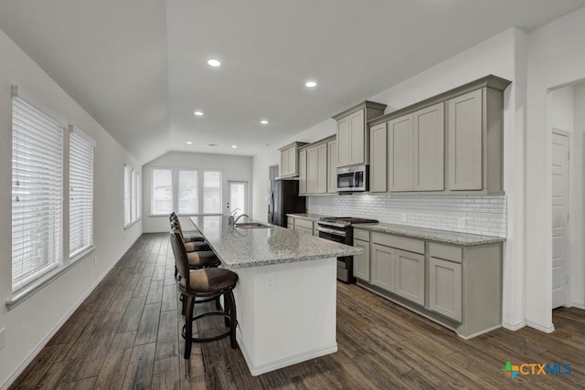 kitchen featuring a kitchen bar, appliances with stainless steel finishes, gray cabinets, an island with sink, and light stone countertops