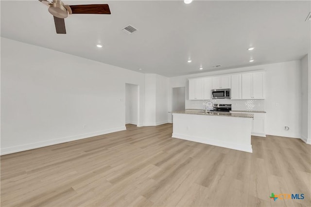 kitchen with an island with sink, white cabinets, backsplash, stainless steel appliances, and light hardwood / wood-style flooring