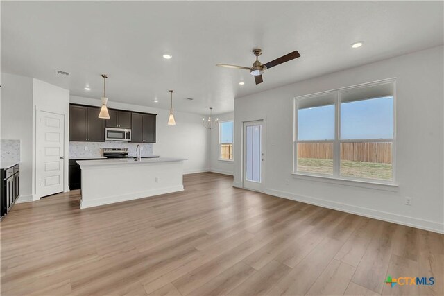 kitchen with an island with sink, white cabinets, backsplash, stainless steel appliances, and light hardwood / wood-style flooring