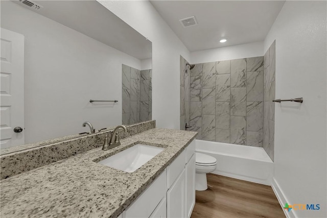 full bathroom with tiled shower / bath combo, vanity, hardwood / wood-style floors, and toilet