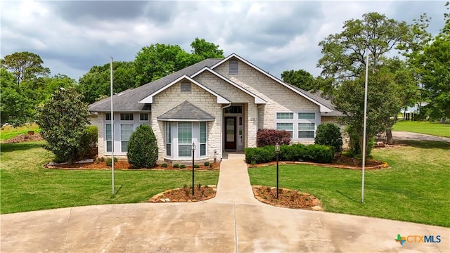 view of front of home featuring roof with shingles, a front yard, and stone siding