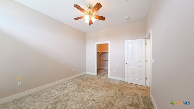 unfurnished bedroom featuring a walk in closet, a ceiling fan, baseboards, carpet floors, and a closet