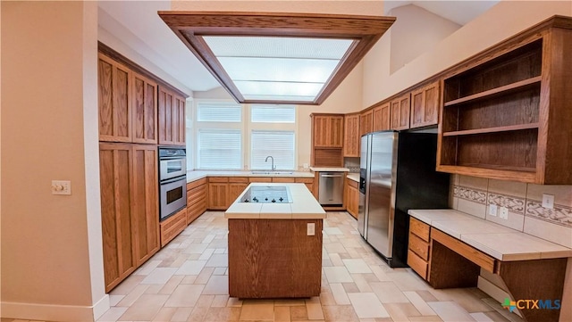kitchen featuring open shelves, appliances with stainless steel finishes, a sink, tile counters, and a center island
