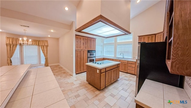 kitchen with stainless steel double oven, a notable chandelier, a sink, light countertops, and a center island