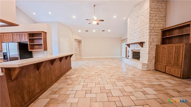 kitchen with ceiling fan, a breakfast bar area, tile countertops, stainless steel refrigerator with ice dispenser, and open shelves
