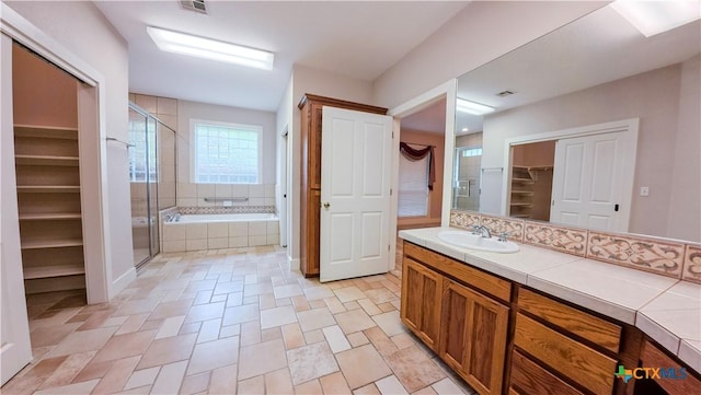 bathroom featuring a walk in closet, a garden tub, visible vents, a stall shower, and vanity