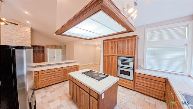 kitchen with brown cabinets, ceiling fan with notable chandelier, stainless steel appliances, tile countertops, and lofted ceiling