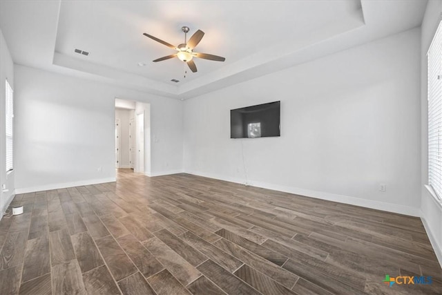 292 Scenic Cyn, New Braunfels, TX 78132 - unfurnished living room featuring a raised ceiling, a ceiling fan, dark wood-style floors, and healthy amount of natural light
