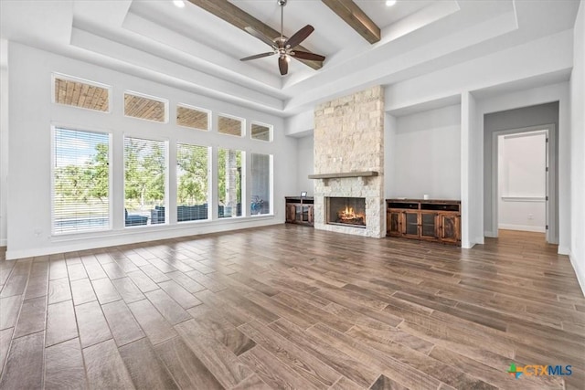 292 Scenic Cyn, New Braunfels, TX 78132 - unfurnished living room featuring a raised ceiling, wood finished floors, ceiling fan, a towering ceiling, and a stone fireplace