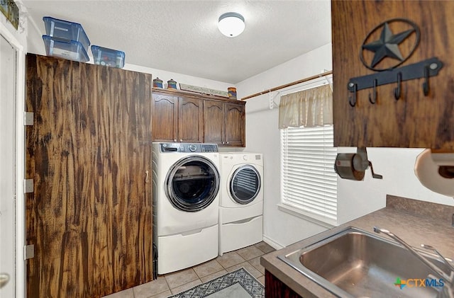 clothes washing area featuring sink, light tile patterned floors, cabinets, washer and dryer, and a textured ceiling