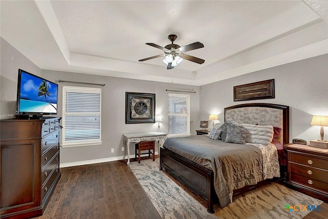 bedroom with dark wood-type flooring, ceiling fan, a raised ceiling, and multiple windows