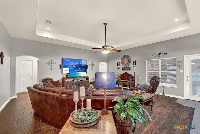 living room with dark hardwood / wood-style floors, ceiling fan, and a tray ceiling