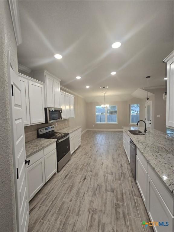 kitchen with light stone countertops, white cabinetry, appliances with stainless steel finishes, and decorative light fixtures