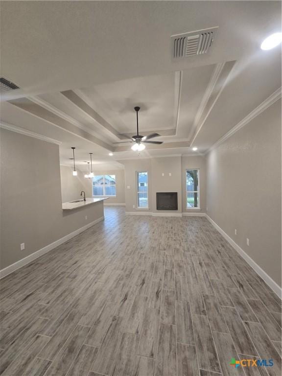 unfurnished living room with visible vents, a raised ceiling, a ceiling fan, and wood finished floors