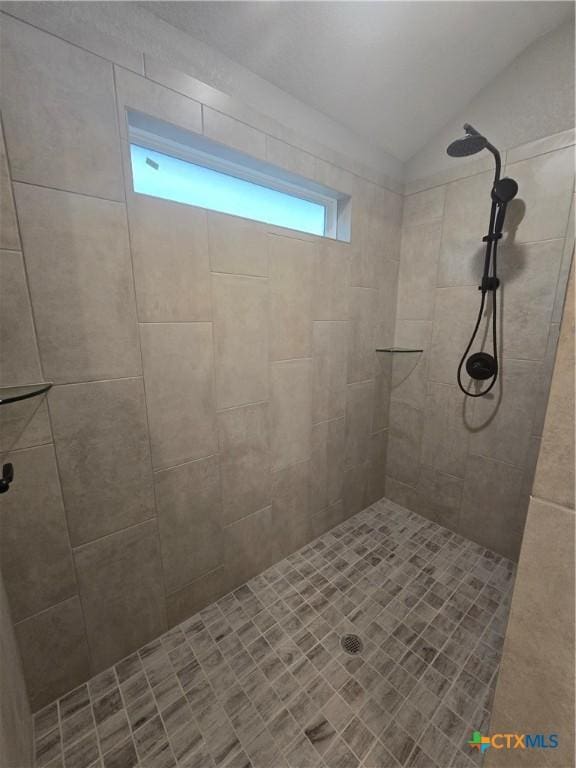 bathroom featuring lofted ceiling and tiled shower