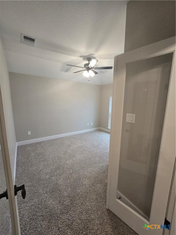 empty room featuring carpet, visible vents, ceiling fan, and baseboards