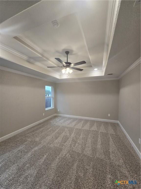 empty room with ceiling fan, carpet flooring, baseboards, ornamental molding, and a raised ceiling