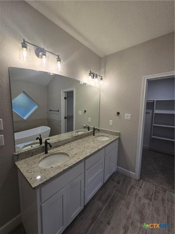 full bath featuring wood finish floors, a sink, a spacious closet, and double vanity