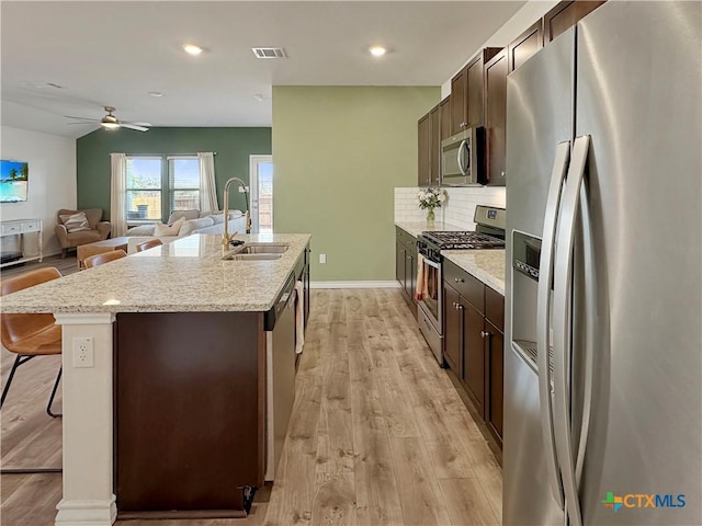 kitchen with an island with sink, sink, a kitchen bar, light hardwood / wood-style floors, and stainless steel appliances