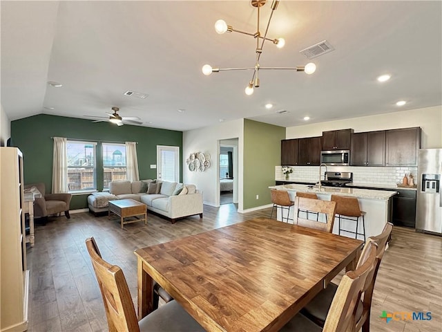 dining space featuring hardwood / wood-style flooring, vaulted ceiling, and ceiling fan with notable chandelier