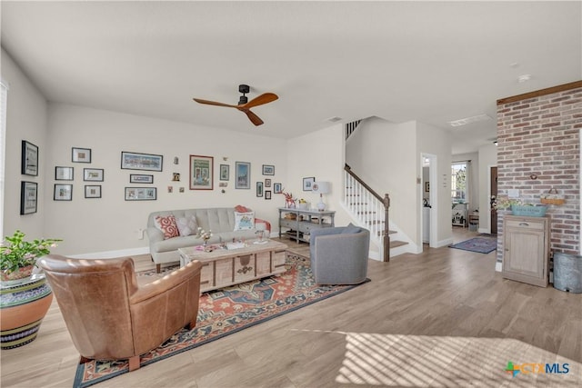 living area with wood finished floors, baseboards, visible vents, ceiling fan, and stairs