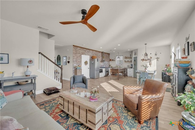 living area with visible vents, baseboards, light wood-style flooring, stairs, and ceiling fan with notable chandelier